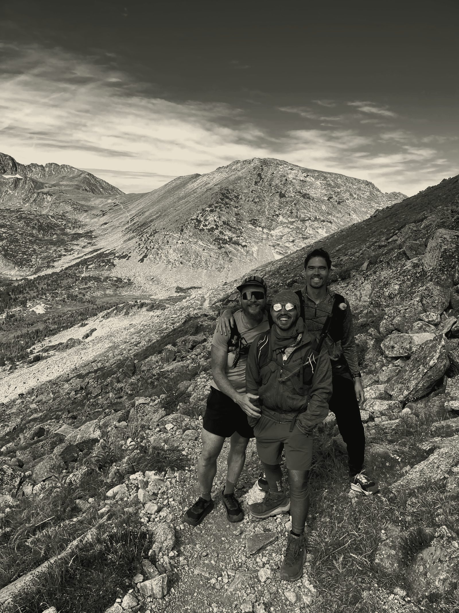 Three men on a high mountain traverse, packs and vests on, ridgeline behind them